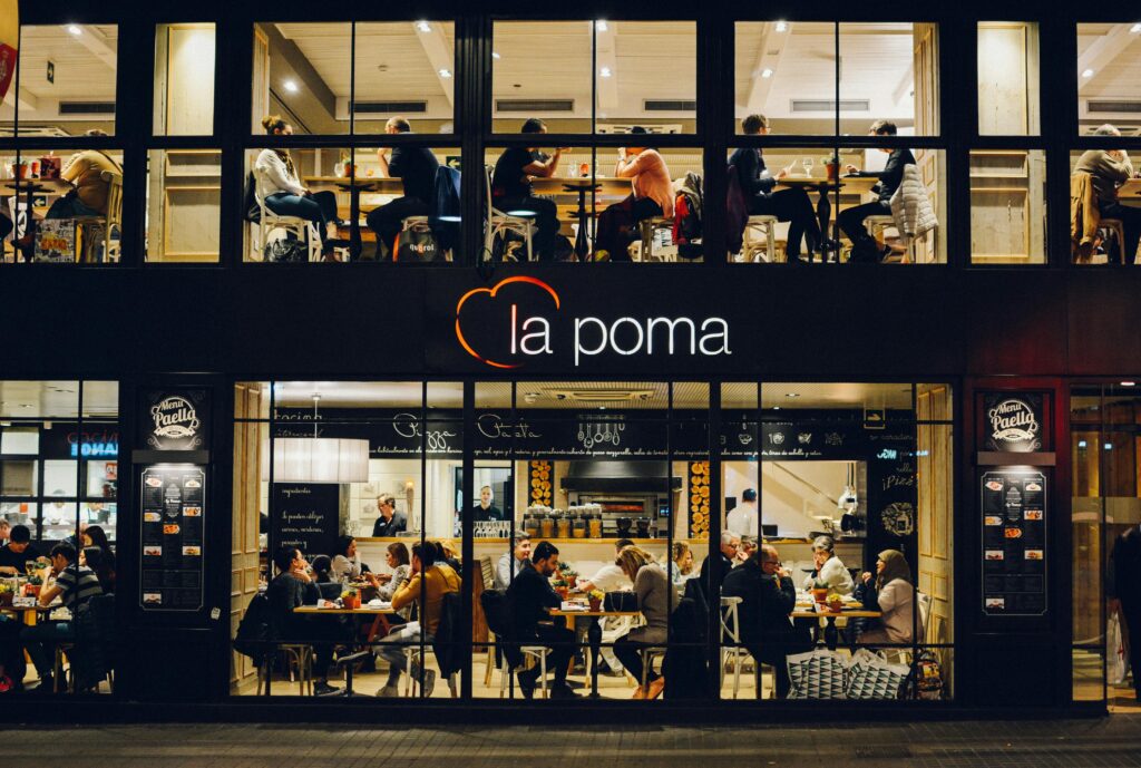 People enjoying a meal indoors at La Poma restaurant in Barcelona, Spain. Warm ambiance and lively atmosphere.